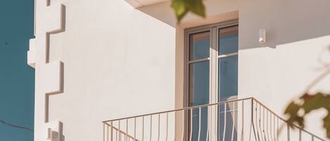 A white building with a balcony featuring a metal railing and a red chair.