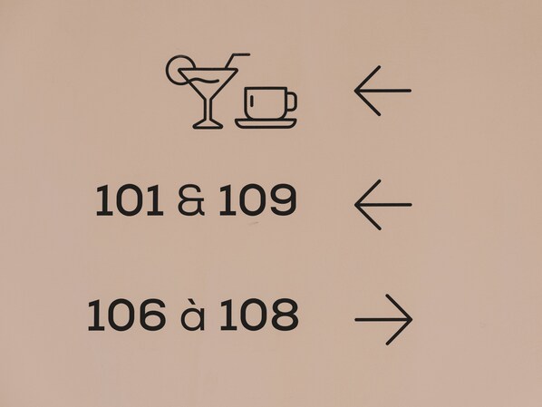 A directional sign with a cocktail icon and a coffee cup, indicating directions to rooms 101 & 109 and 106 to 108.