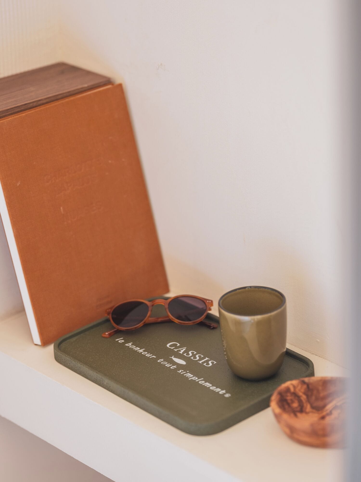 Una estantería con un libro marrón, unas gafas de sol y una taza.