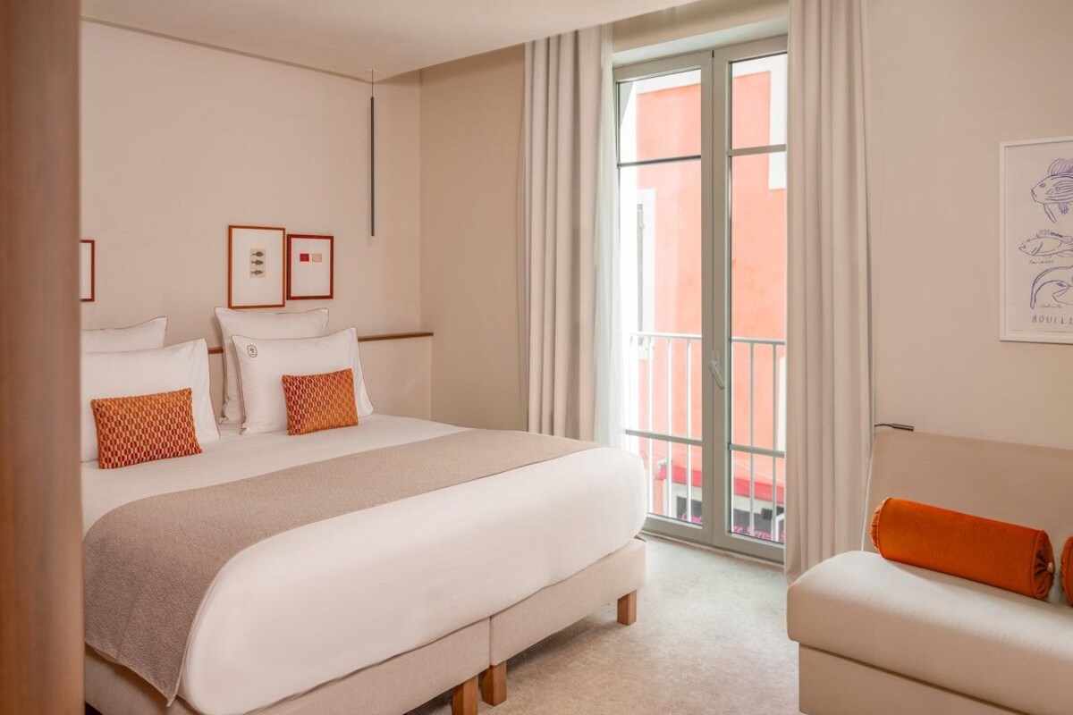 A hotel room with a large bed, a small sofa, and a balcony with a view.