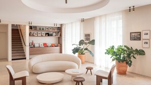 A spacious living room with a curved sofa, round coffee tables, and wooden chairs. A staircase leads to an upper level. - Hôtel Liautaud Cassis by Germain Collection (Cassis)