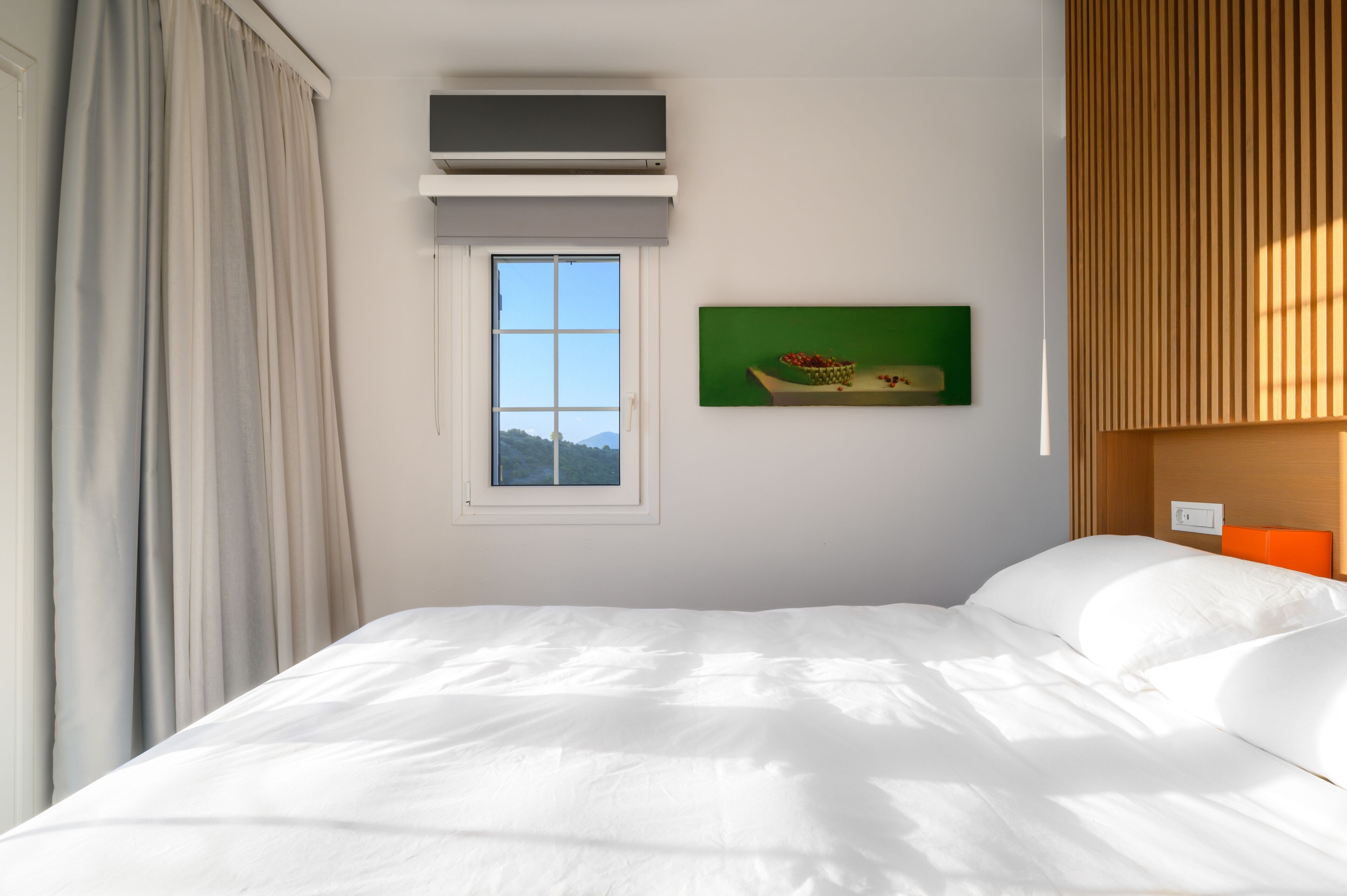 Een hotelkamer met een bed, een raam, een airconditioningapparaat, een schilderij en een wand van hout.
