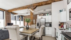 A modern kitchen with white cabinets, a stainless steel refrigerator, and a dining area with a wooden table and chairs.