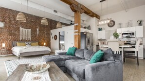 A modern living room with a grey sectional sofa, a wooden coffee table, and a brick wall.