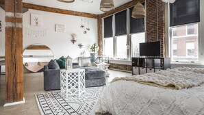 A modern living room with a large bed, grey sofas, a white coffee table, and a TV on a black stand.