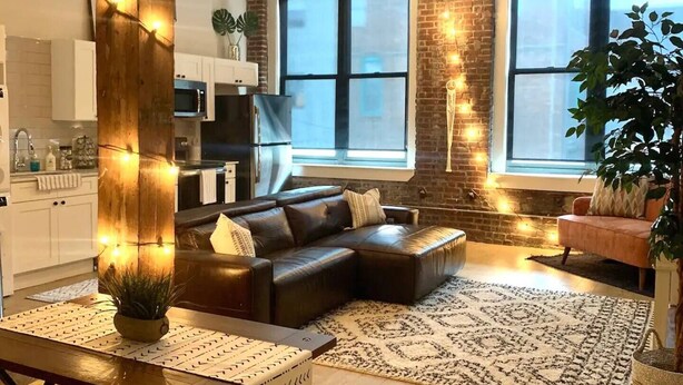 Ein modernes Wohnzimmer mit einer großen Eckcouch, einem Essbereich mit Holztisch und -stühlen sowie einer Küche im Hintergrund.