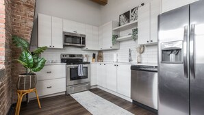 A modern kitchen with white cabinets, stainless steel appliances, and a brick accent wall. - Loft in the Rivermarket District! Rooftop access and DT KC views. Walk to City Market, local coffee shops, restaurants, shops or hop on the free streetcar just steps away. Minutes from  P&L, T-Mobile, Crossroads, Plaza. 10 min drive to stadiums. (Kansas City)
