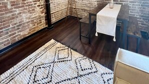 A room with exposed brick walls, a wooden floor, a patterned rug, a small table with a white tablecloth, and a floor lamp. - Loft in the Rivermarket District! Rooftop access and DT KC views. Walk to City Market, local coffee shops, restaurants, shops or hop on the free streetcar just steps away. Minutes from  P&L, T-Mobile, Crossroads, Plaza. 10 min drive to stadiums. (Kansas City)
