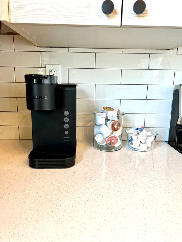 Une cuisine avec une machine à café noire, un bocal en verre contenant des objets blancs et un bol rempli d’articles blancs.