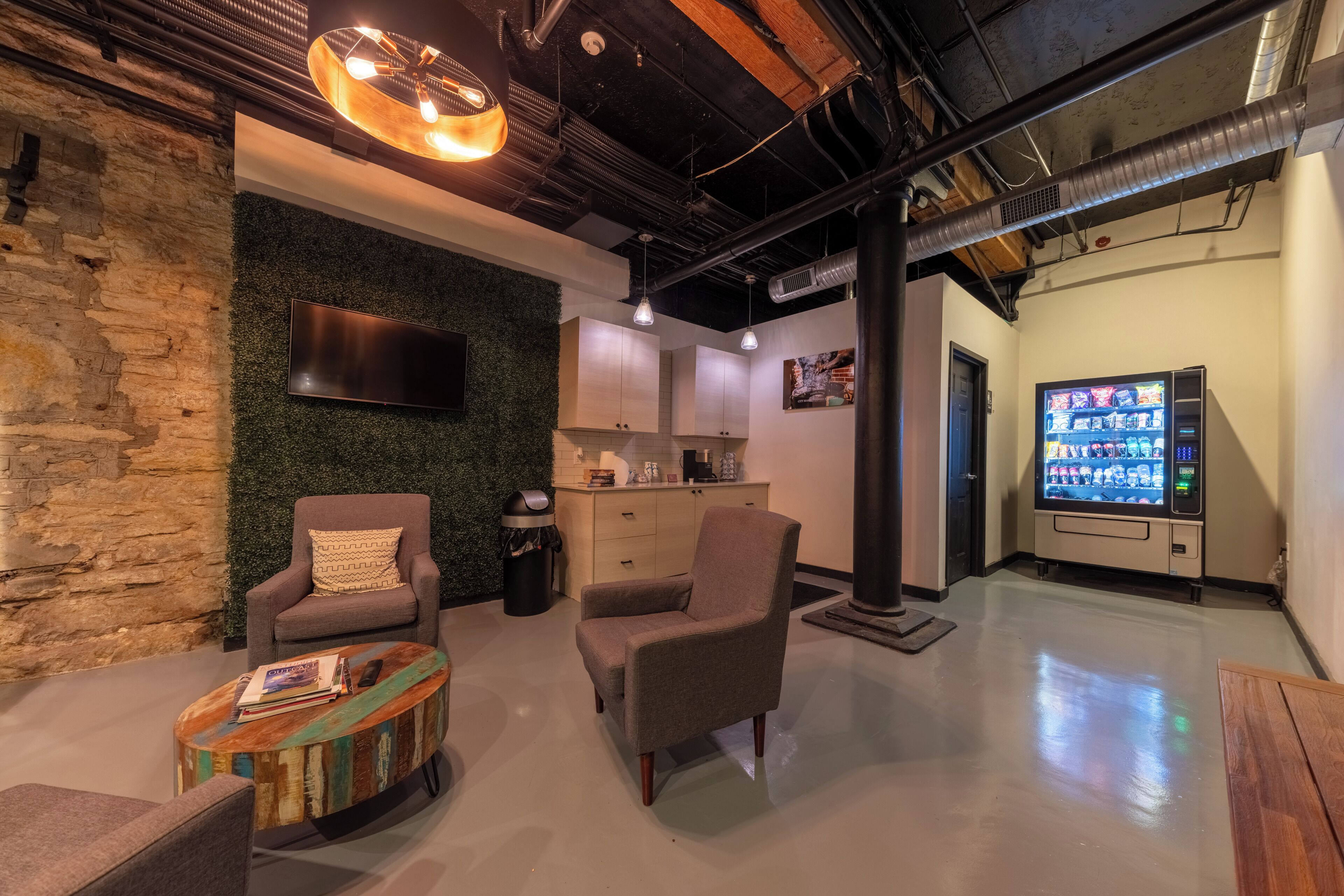 A modern interior with a stone wall, a flat-screen TV, a vending machine, and a seating area with a coffee table.