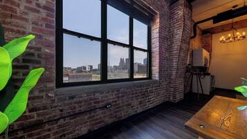 A room with a large window, brick walls, a wooden floor, and a chandelier.