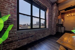 A room with a large window, brick walls, a wooden floor, and a chandelier. - Exposed brick, wood beams, & chic touches give this loft serious style. Enjoy skyline views from the rooftop, a full kitchen with coffee bar, king bed, on-site gym, & quick access to the free KC streetcar. Walk to shops/dining, and the City Market! (Kansas City)
