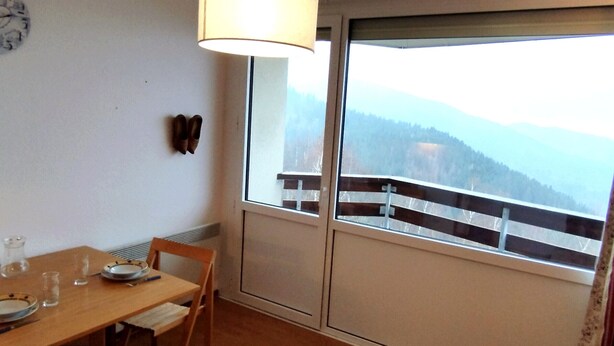 Un coin repas avec une table en bois, des chaises et une lampe suspendue. Une fenêtre offre une vue sur un paysage montagneux.