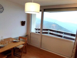 Un'area pranzo con un tavolo di legno, sedie e una lampada a sospensione. Si vede una finestra con vista su un paesaggio montano.