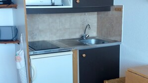 Une cuisine de taille réduite, équipée d’un évier, d’un petit réfrigérateur et d’un meuble en bois.