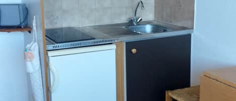 A compact kitchen with a sink, a small refrigerator, and a wooden cabinet.