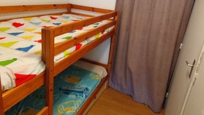 Un lit superposé avec une literie aux couleurs vives, un plancher en bois et une porte dotée d’une poignée.