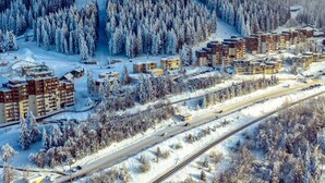 Un quartier résidentiel enneigé, avec des immeubles à plusieurs étages, une voie ferrée et une forêt dense.