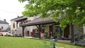 Un bâtiment en pierre avec un toit en tuiles, un espace extérieur aménagé pour s’asseoir et une pelouse verdoyante.