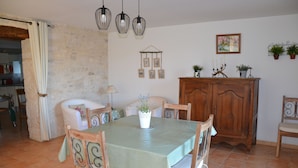 Un coin repas avec une table dressée pour quatre personnes, entourée de chaises en bois agrémentées d’éléments en métal. Un buffet en bois, orné d’un miroir et d’objets décoratifs, est adossé au mur.