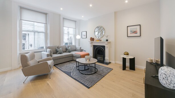 A modern living room with a sectional sofa, a round coffee table, a fireplace, and a large window. - Urban Chic - Drury (London)