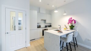 A modern kitchen with white cabinetry, a central island with bar stools, and a pendant light above the island. - Urban Chic - Drury (London)