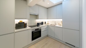 A modern kitchen with white cabinetry, a built-in oven, a microwave, and a skylight. - Urban Chic - Drury (London)