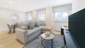A modern living room with a grey sofa, a dining table with chairs, a round coffee table, and a TV on a stand. - Urban Chic - Drury (London)