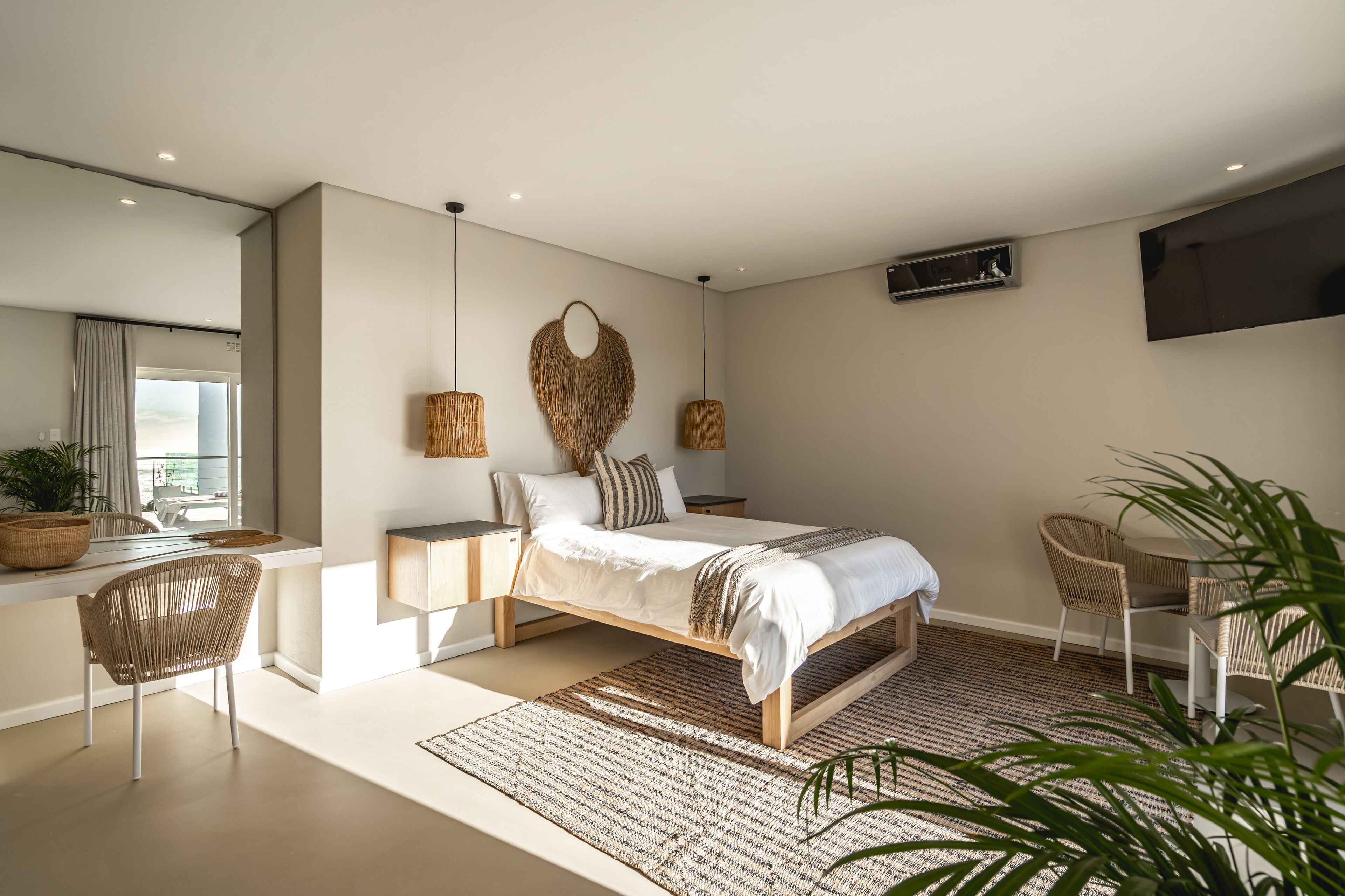Un dormitorio moderno con cama, mesitas de noche, televisor y zona de comedor.