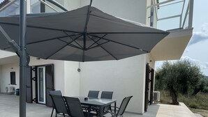 An outdoor patio with a table and chairs, a large umbrella, and a building with a modern design.