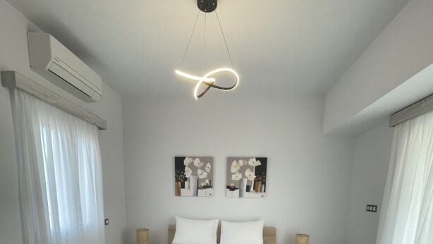 A modern bedroom with a wooden bed, white bedding, two wall-mounted paintings, and a ceiling light fixture.