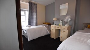 A hotel room with two beds, a desk with a lamp, a mirror, and a fan.