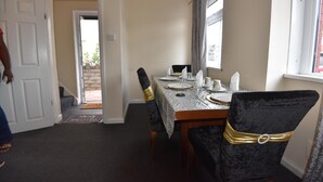 A dining area with a table set for four, chairs with gold sashes, a window with curtains, and a door leading outside.