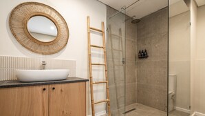A bathroom with a white sink, wooden cabinets, a round mirror, a glass shower enclosure, and a bamboo ladder.