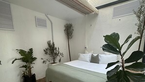 Un dormitorio con cama, una planta grande en maceta y un suelo estampado.