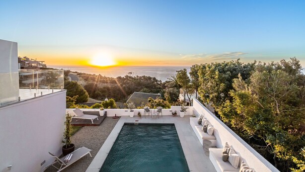Una piscina en la azotea con sillones de descanso y vistas al atardecer sobre el océano.