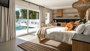 Ein modernes Schlafzimmer mit einem großen Bett, Blick auf einen Swimmingpool und einer Küchenzeile.