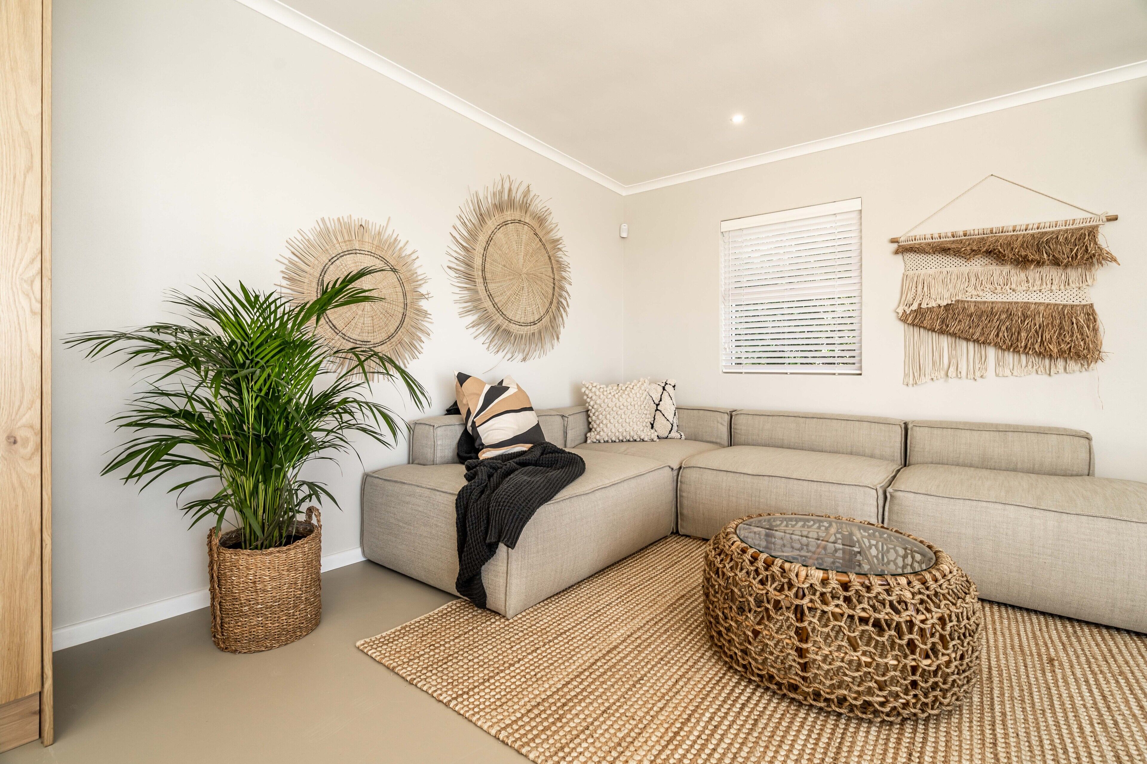 A modern living room with a sectional sofa, a large potted plant, and decorative wall hangings.