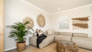 A modern living room with a sectional sofa, a large potted plant, and decorative wall hangings. - View 16 | Serinity Skyline Penthouse | 3 Bedroom (Cape Town)