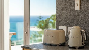 A kitchen with two Smeg appliances on a granite countertop, a wooden cabinet below, and a view of the ocean through a glass door. - View 16 | Serinity Skyline Penthouse | 3 Bedroom (Cape Town)