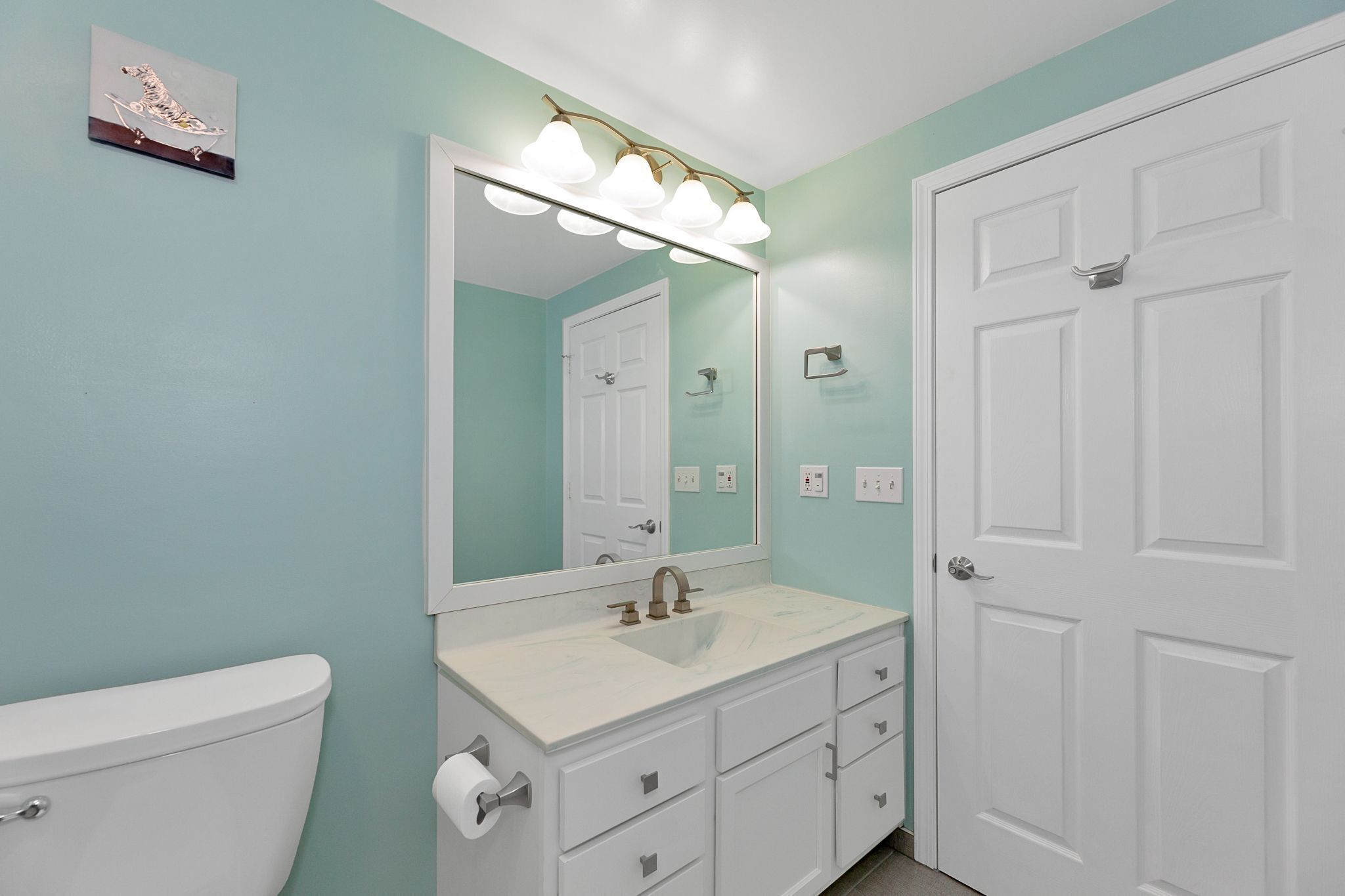 A bathroom with a white toilet, a sink with a mirror above it, and a door to the right.
