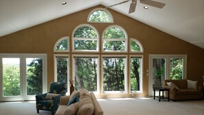 Un ampio soggiorno con soffitto alto, grandi finestre e una ventola a soffitto.