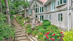 Un edificio in legno con diverse finestre e un tetto rosso, circondato da un giardino con dei gradini che portano all'ingresso.