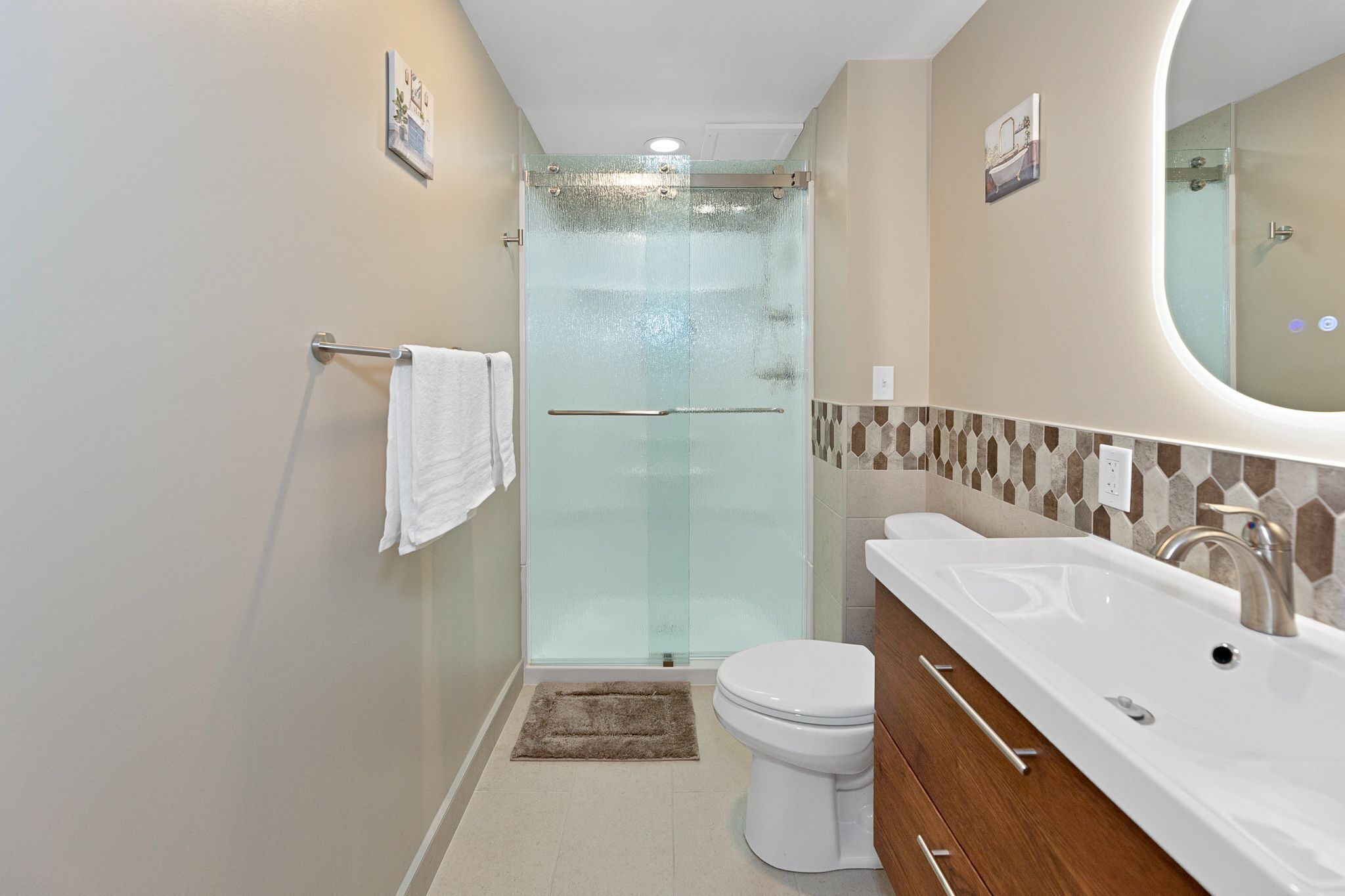 A modern bathroom with a glass-enclosed shower, a white toilet, and a large sink with a mirror.