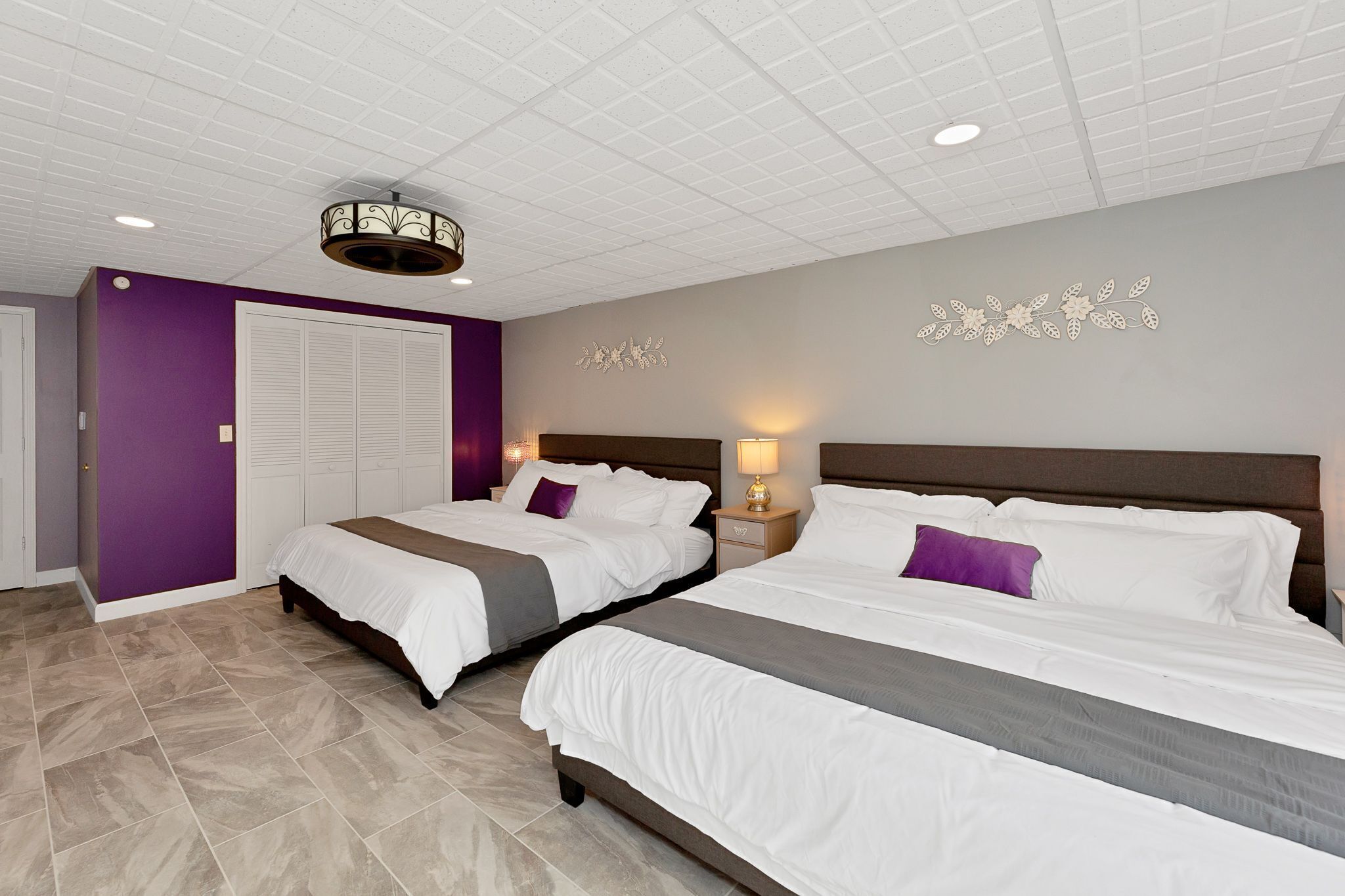 A hotel room with two beds, a ceiling light fixture, and a decorative wall piece.