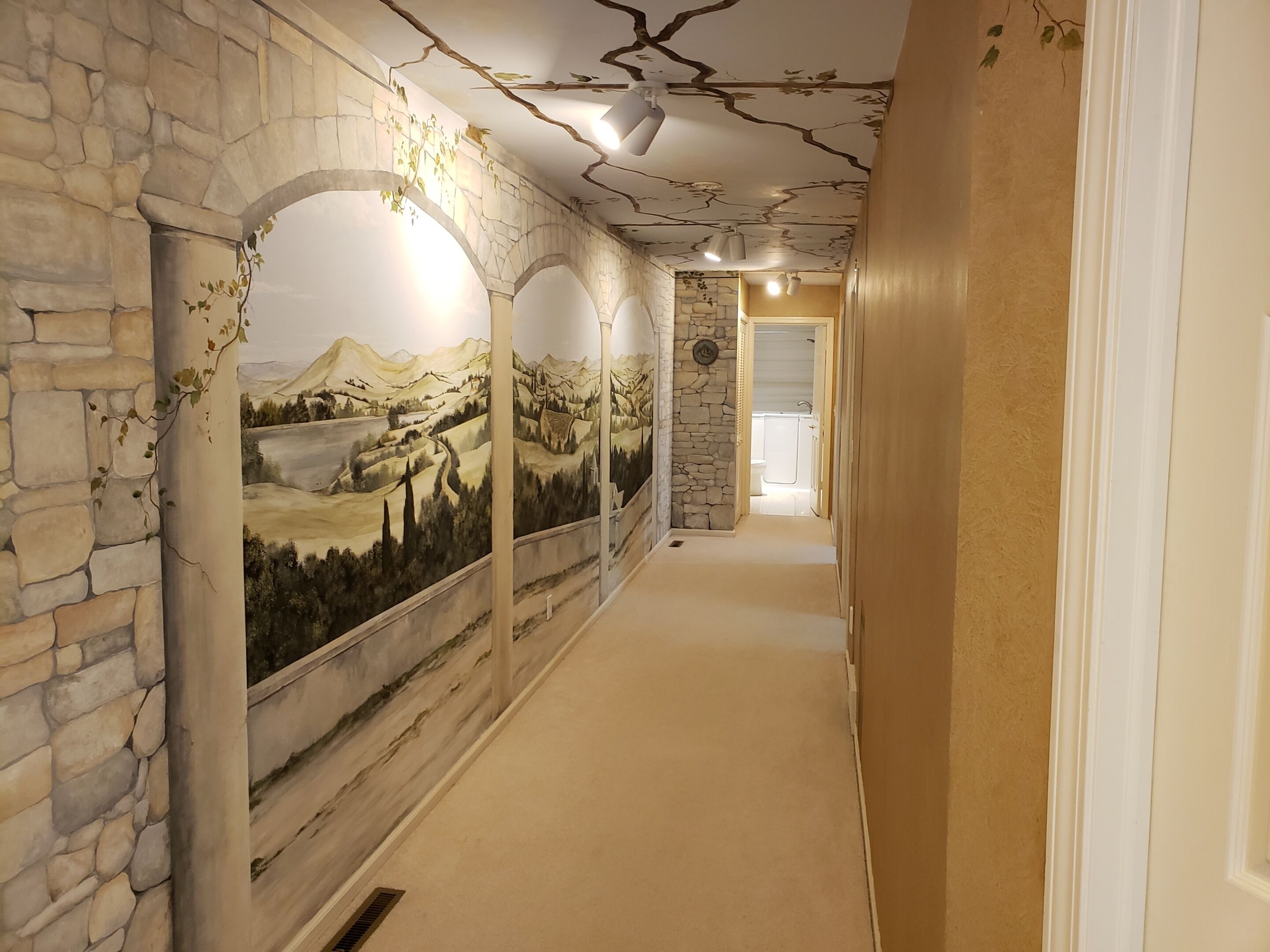 Ein Flur mit Steinwänden, einem Wandgemälde und Blick ins Badezimmer.