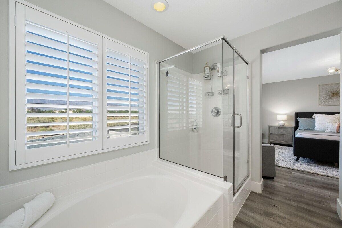 A modern bathroom with a glass-enclosed shower, a bathtub, and a window with white blinds.