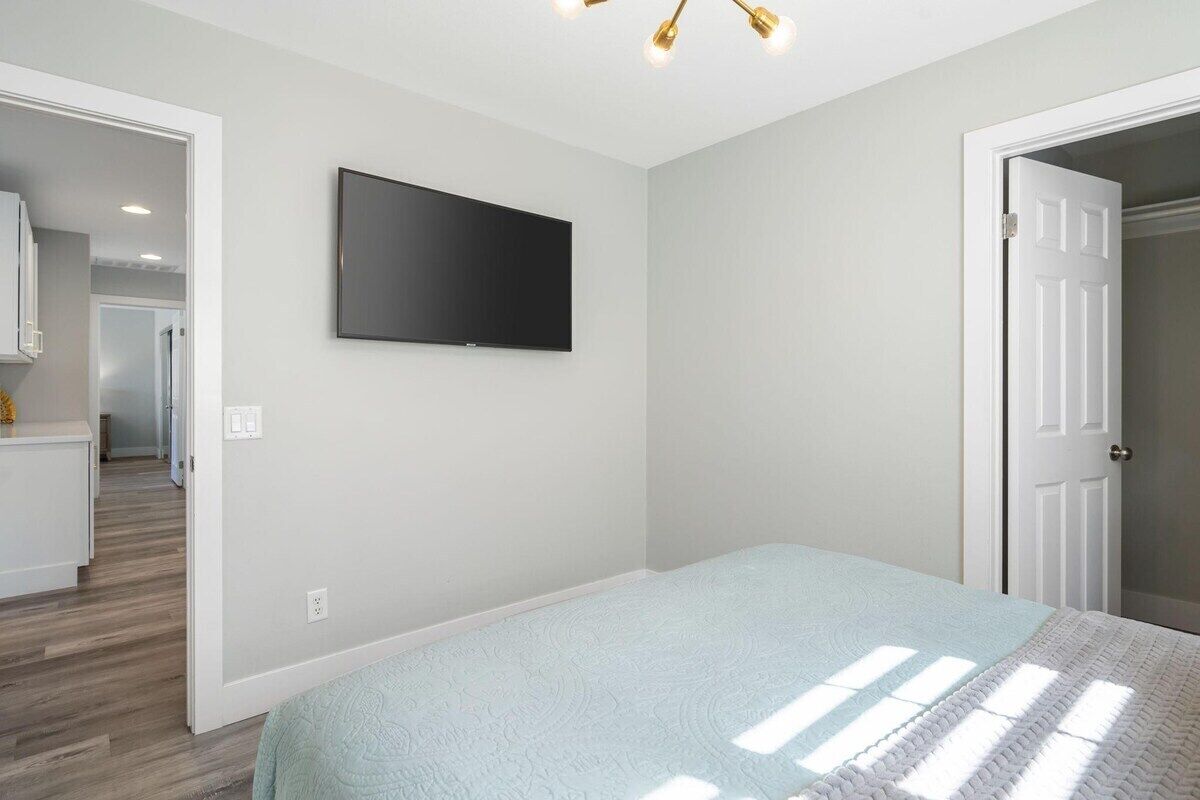 Een slaapkamer met een bed, een aan de muur bevestigde televisie en een deur naar een andere kamer.