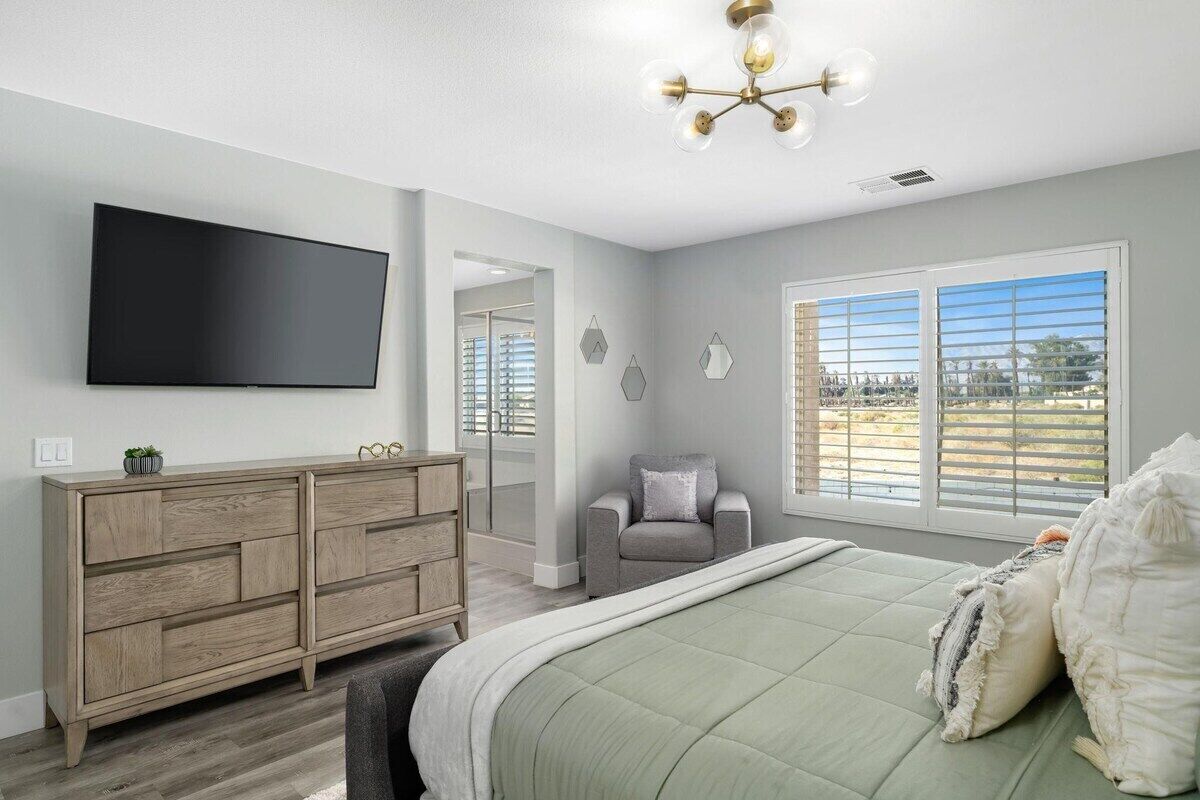 Une chambre à coucher avec un grand lit, une commode, un téléviseur et une fenêtre avec des stores.