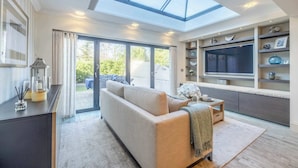 Una sala de estar moderna con un sofá, una mesa de centro y un televisor en un mueble empotrado. Hay una puerta de vidrio que da a un espacio exterior.